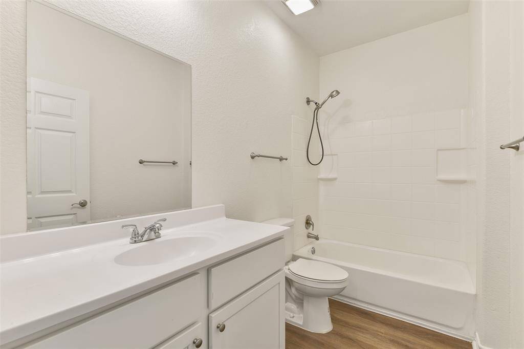 The en suite master bathroom features a clean, modern design with a white vanity, a large mirror, and a shower-tub combo. The walls and fixtures are white, creating a bright and spacious feel. The wood-look flooring adds warmth to the space.