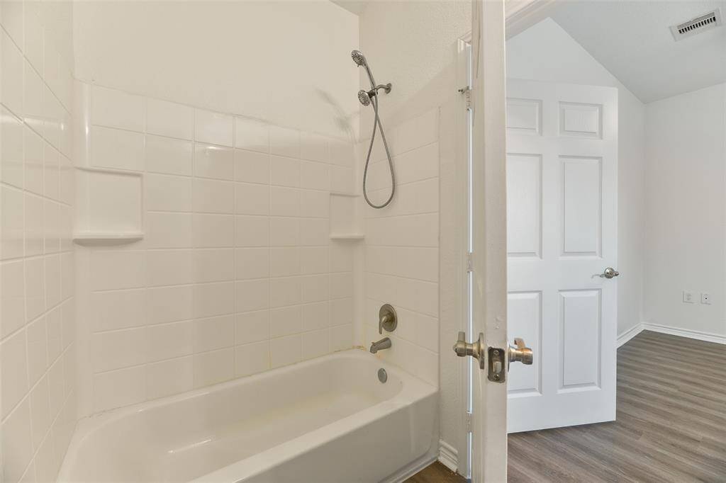 This bedroom services the secondary bedrooms with a clean, modern all-white vanity, a basin sink with a chrome faucet, neutral wall colors, and a combination bathtub and shower with a white tile surround.