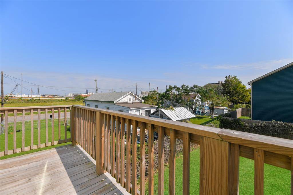 Step out onto the wooden deck overlooking a lush green backyard, with views of neighboring houses and a clear blue sky, offering a pleasant outdoor space for relaxation.