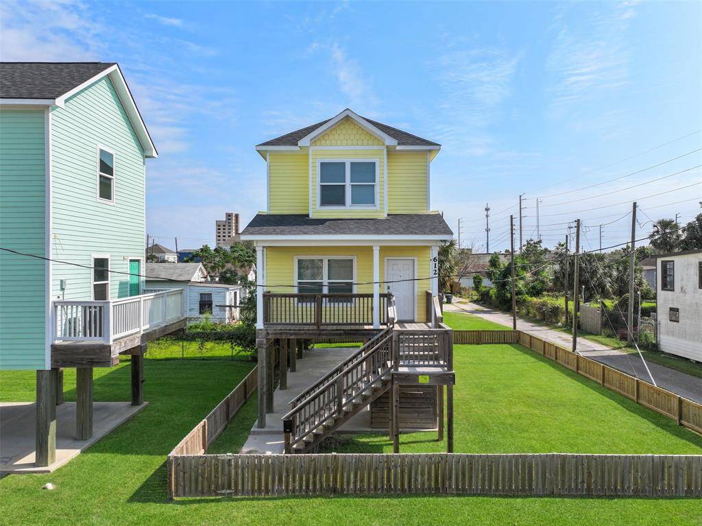 This charming two-story home features a vibrant yellow exterior with a spacious front porch and elevated entrance. The property includes a well-maintained lawn surrounded by a wooden fence, offering a cozy backyard space. The neighboring lot (included in the fenced area) is also for sale separately!