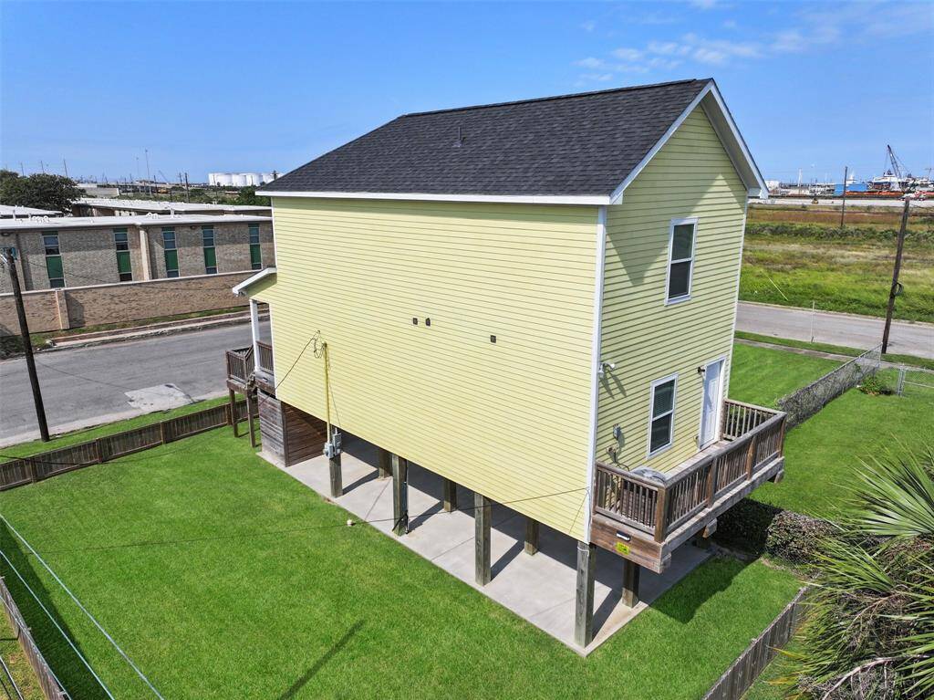An aerial view of the back of the home highlights the rear balcony and the ample space beneath the home. The lot beside the home (included in the fenced area) is also for sale separately.