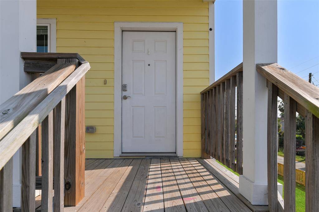 This photo shows a welcoming front entry with a cheery yellow exterior, a white door, and a wooden porch railing, creating a charming and inviting entrance.