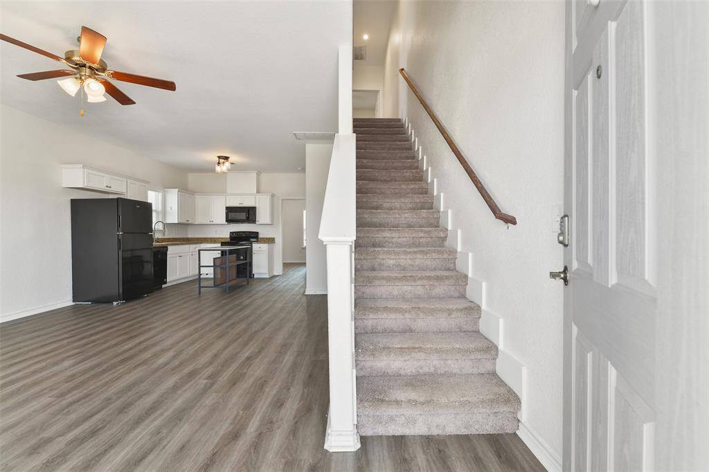enter directly into this bright and open living space with modern luxury vinyl plank flooring. The kitchen features white cabinetry, black appliances, and ample counter space. A carpeted staircase leads to the upper level bedrooms, and there's a ceiling fan in the living area for added comfort.