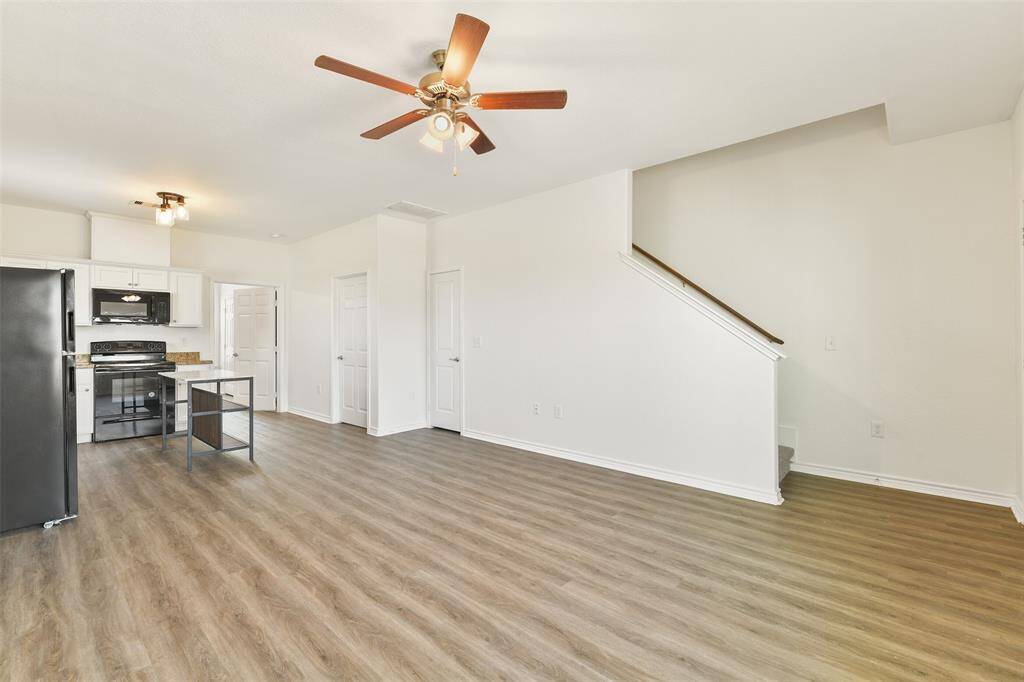 The bright, open-concept living area with luxury vinyl plank flooring flows seamlessly into the modern kitchen with white cabinetry, granite countertops, black appliances, and a moveable island.