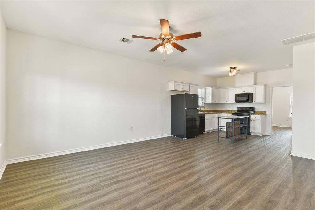 The bright, open-concept living area with luxury vinyl plank flooring flows seamlessly into the modern kitchen with white cabinetry, granite countertops, black appliances, and a moveable island.