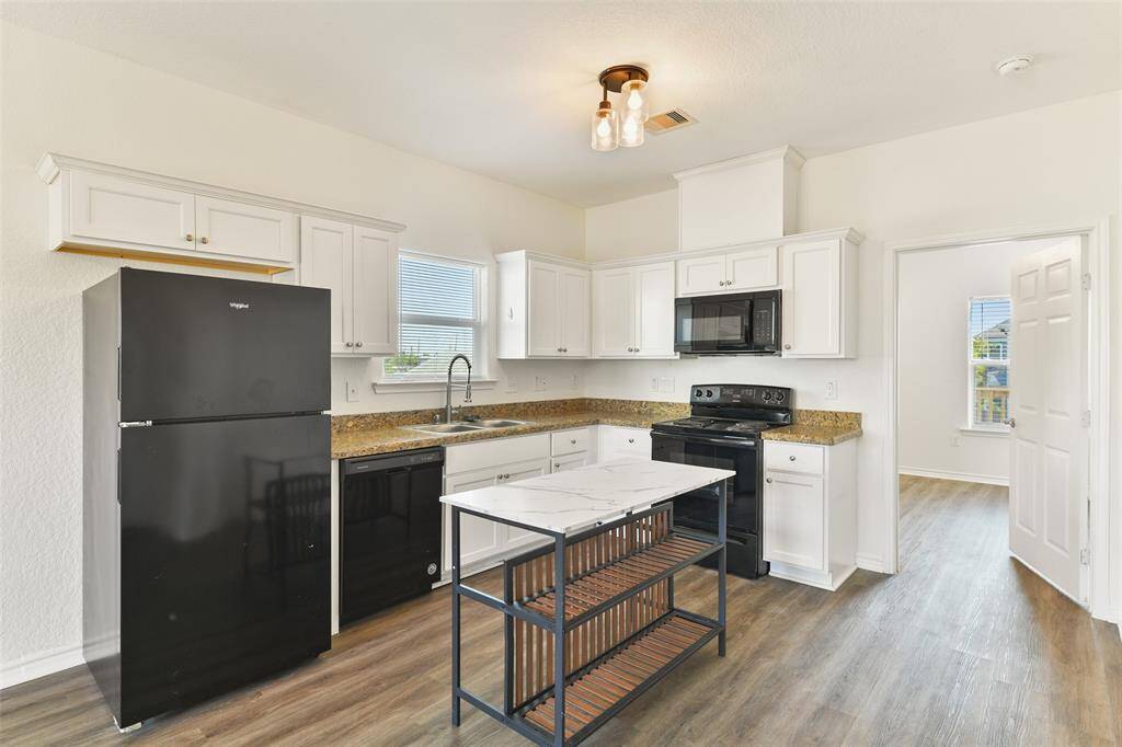 Enter the light & bright kitchen with modern black appliances, white cabinetry, granite countertops, and a moveable central island with a marble-inspired countertop. Luxury vinyl plank flooring adds warmth & functionality.