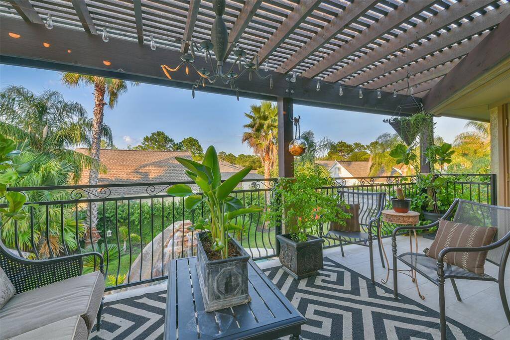 Large balcony area covered with a pergola overlooking the pool and tropical landscaping.