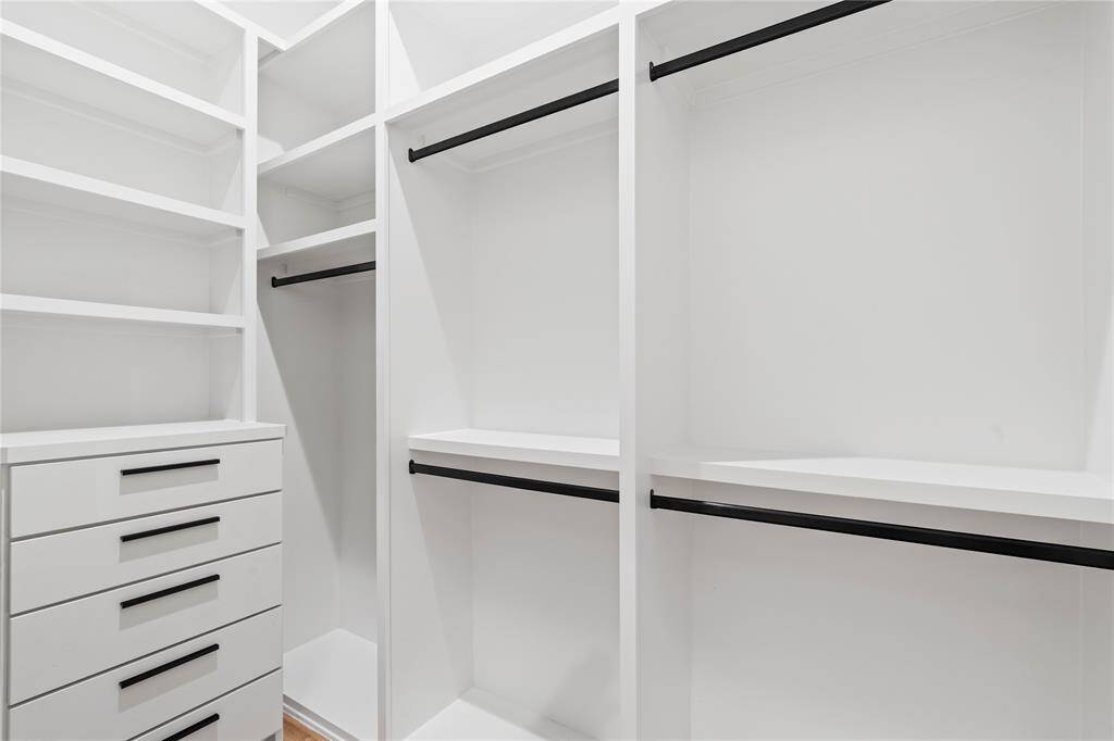 This thoughtfully designed walk-in closet offers a perfect blend of functionality and style, featuring custom shelving, sleek black hardware, and ample storage to keep everything organized and easily accessible.