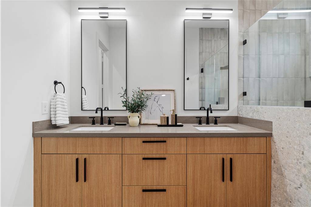 This primary bathroom showcases a seamless blend of modern design and functionality, featuring a spacious double vanity with sleek quartz countertops, custom wood cabinetry, and bold black hardware.
