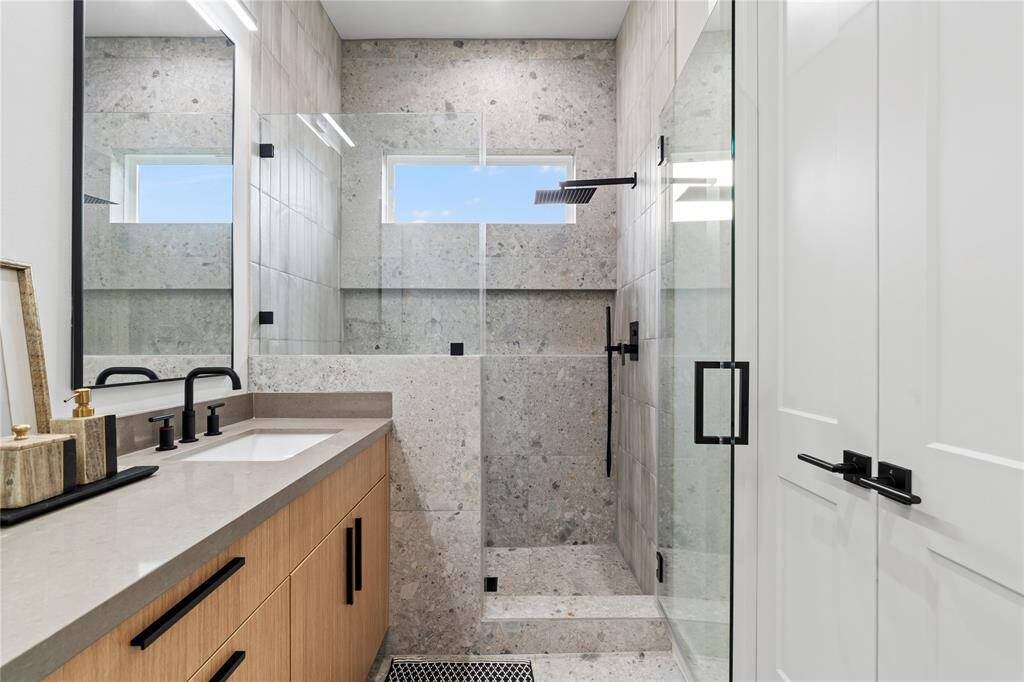 The walk-in shower is elegantly designed with floor-to-ceiling tile, a frameless glass enclosure, and a rainfall showerhead, while strategically placed windows bring in natural light for a spa-like ambiance.