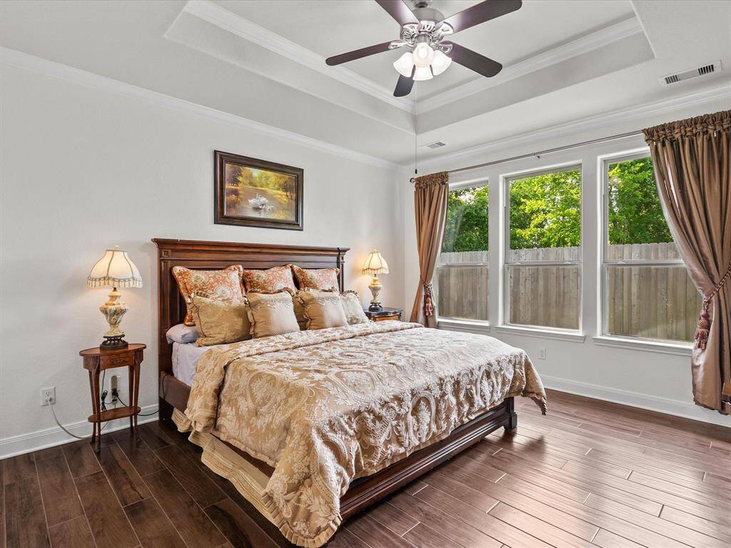 Primary suite is spacious featuring wood-look tile flooring, crown molding, tray ceiling, and ample windows for views of the trees and the birds!