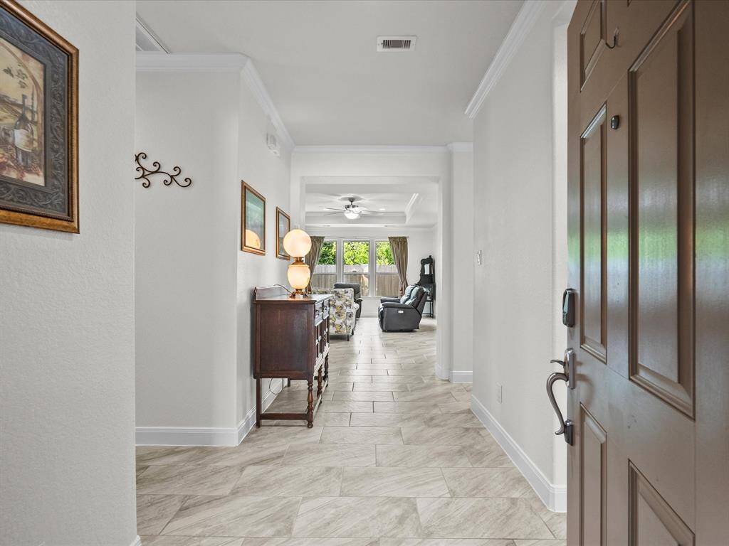 Wide open entry way highlighted by neutral tile flooring and crown molding.