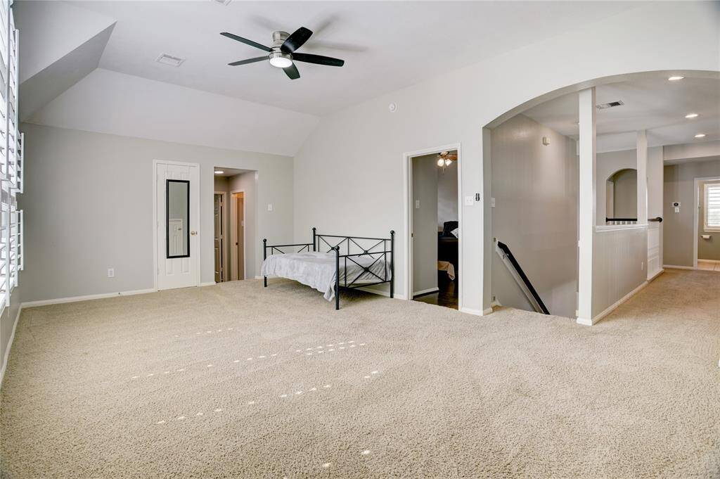 Spacious game room with neutral colors, featuring a ceiling fan, large windows with shutters, and an open layout connecting to other areas. Ideal for an extra versatile living space!
