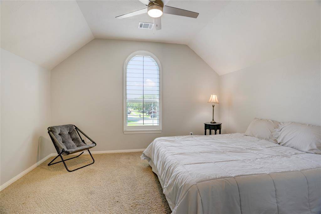 This bedroom features a cozy atmosphere with a vaulted ceiling, soft carpet, and a large arched window for natural light.