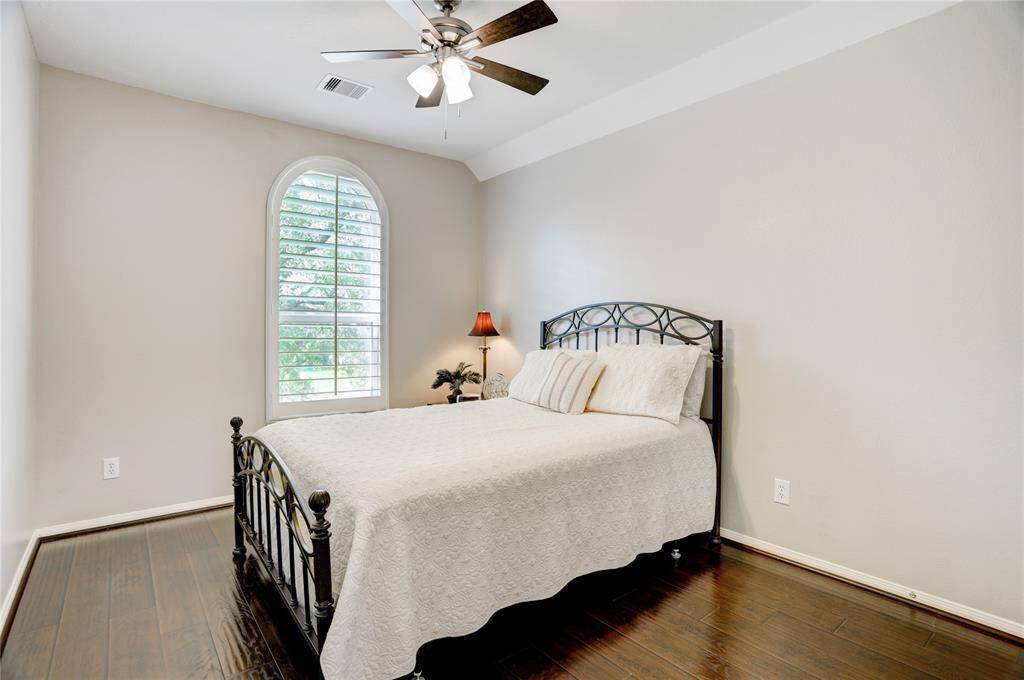 This cozy bedroom features flooring, and a large window with shutters for natural light. A ceiling fan provides comfort, and the neutral wall color creates a calm atmosphere.