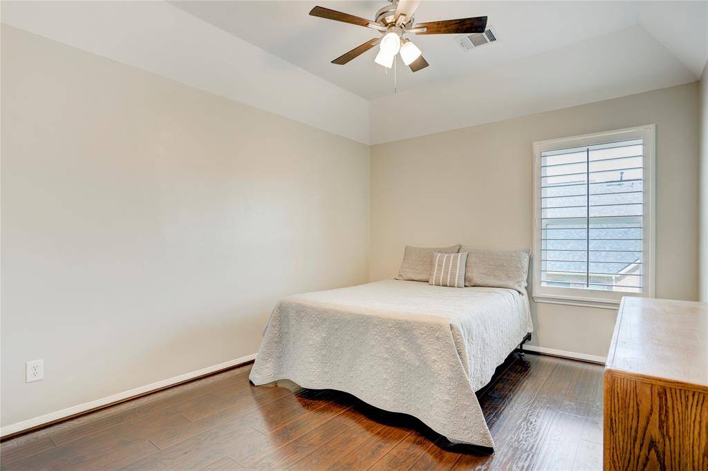 This cozy bedroom features a vaulted ceiling with a ceiling fan, and a window with shutters for natural light.