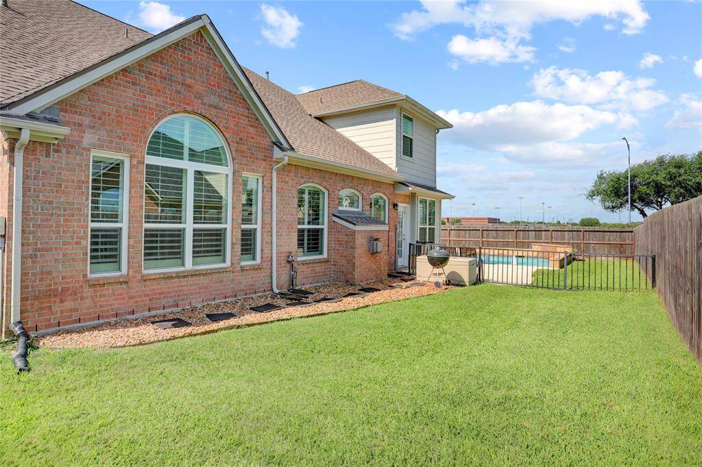 This home showcases a charming brick home with large arched windows, a well-maintained fenced backyard, and pool area, perfect for outdoor relaxation and entertaining.