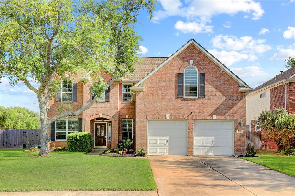 This is a charming two-story brick home with a double garage. It features a well-maintained lawn, mature trees, and a welcoming front entry. The large windows and classic shutters add to its curb appeal.