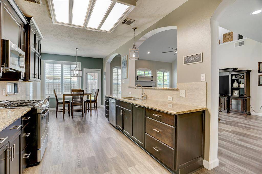 Bright kitchen with granite countertops, dark cabinets, and stainless steel appliances. The open layout flows into a cozy dining area with large windows, and connects to the living room.