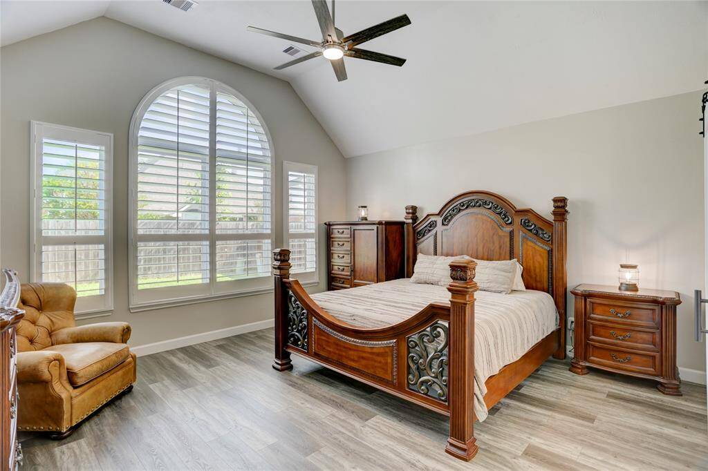 This spacious bedroom features high ceilings and a large arched window with shutters, allowing for plenty of natural light, creating a warm and inviting atmosphere.