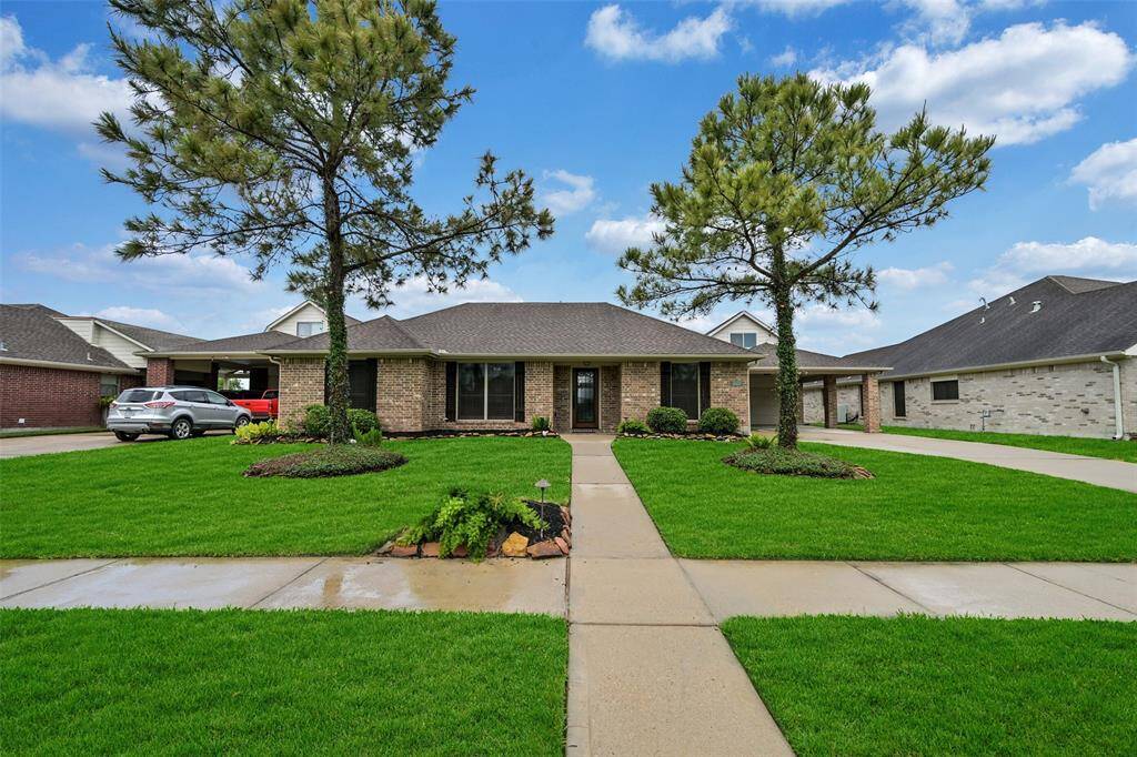 Charming single-story lakefront home in the peaceful Lakeland community in Manvel boasts a classic brick exterior, mature pine trees, freshly mulched and rock-lined landscape beds.
