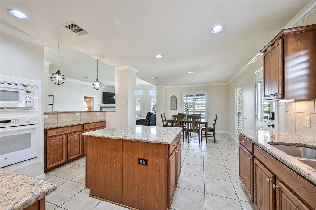 Spacious open-concept layout seamlessly connects the kitchen and dining area, with granite countertops, a central island, breakfast bar seating, and abundant natural light through plantation-shuttered windows.