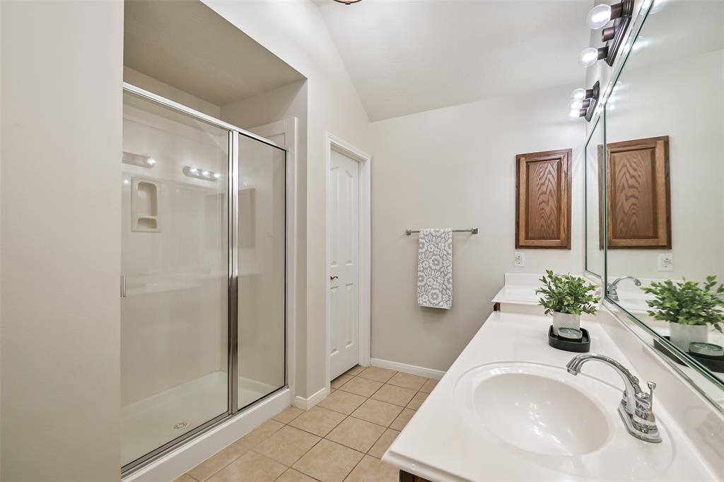 Spacious primary bathroom features dual vanities with a seated makeup area, a full-wall mirror, built-in cabinetry, and a large walk-in shower with sliding glass doors, all finished in neutral tones.