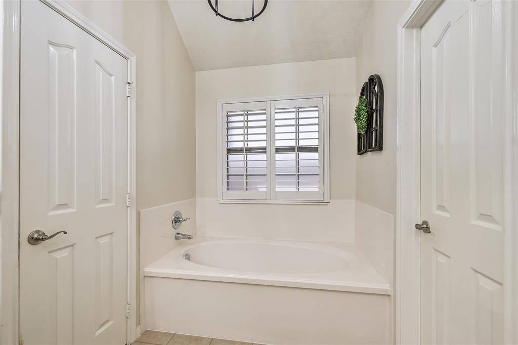 Relax in the large soaking tub nestled between two walk-in closets, with privacy plantation shutters and vaulted ceilings adding a touch of elegance.