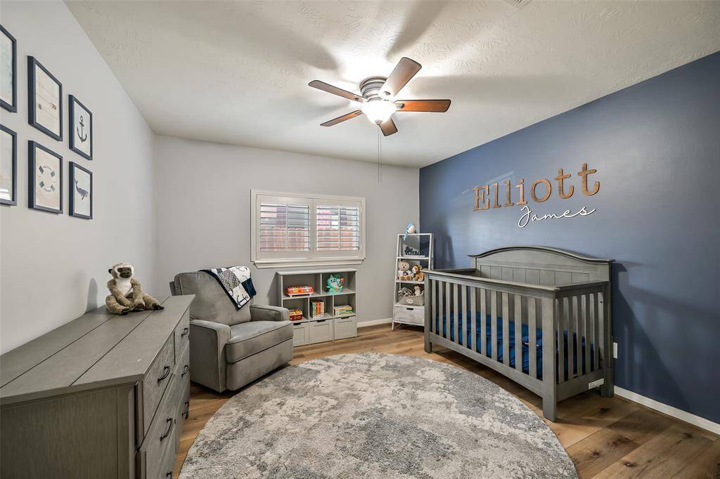 Charming secondary bedroom features wood-look flooring, a bold accent wall, plantation shutters, and a ceiling fan for comfort and style.