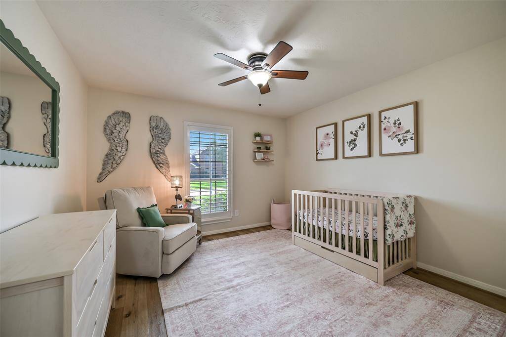 The remaining secondary bedroom boasts wide plank floors, custom wall decor, and a large window with plantation shutters offering serene front yard views.