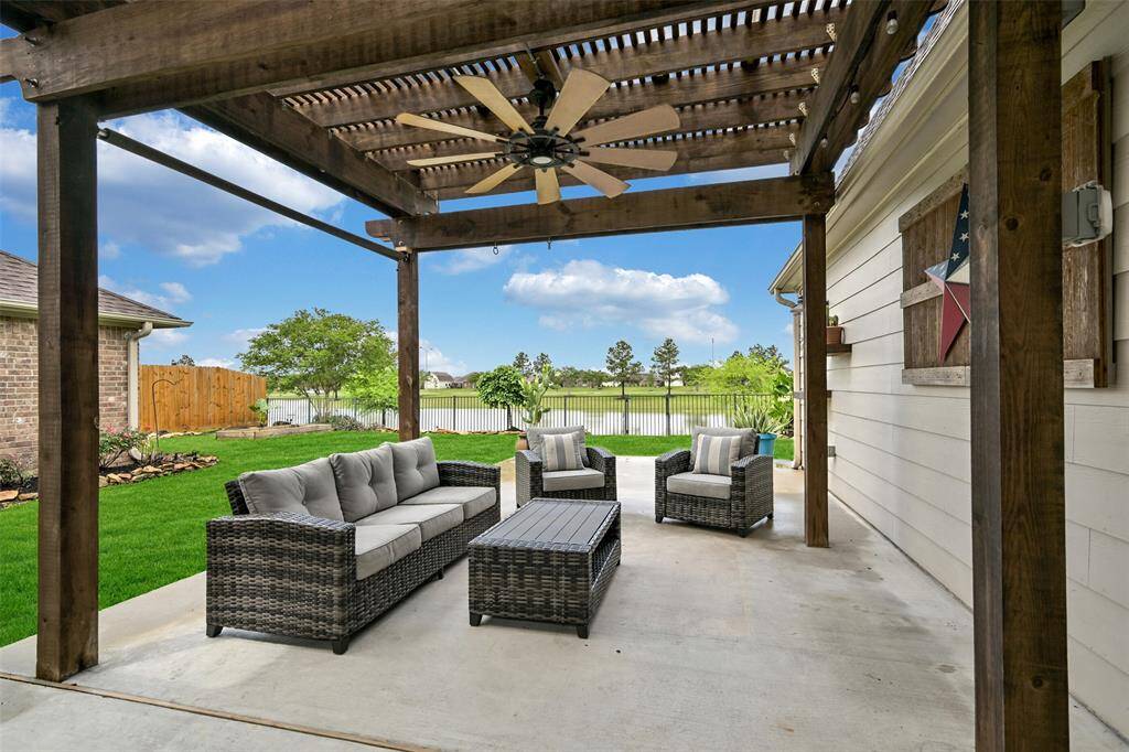 Relax on the beautifully crafted covered patio with a wood pergola, oversized ceiling fan, and relaxing lake views beyond the wrought iron fence — perfect for outdoor entertaining or quiet evenings.