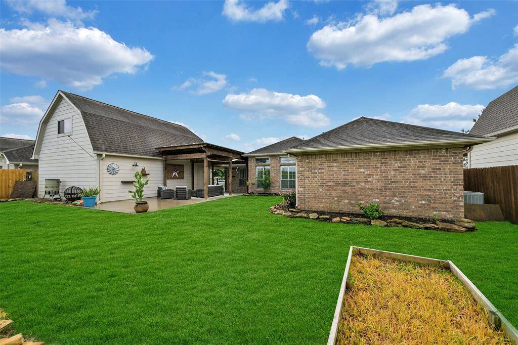 Spacious backyard offers lake views and ample green space, with a raised garden bed and plenty of room to entertain or relax beneath the pergola-covered patio.