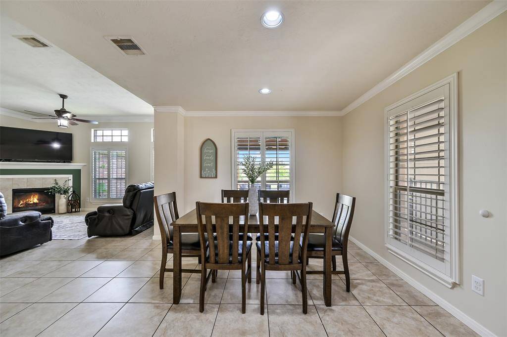 The dining area offers a seamless transition from the living space and features crown molding, plantation shutters, and tile flooring—ideal for everyday meals or entertaining, all with views of the backyard and lake beyond.