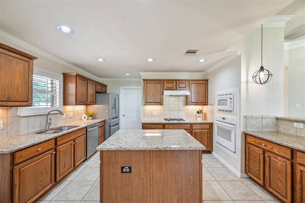 The kitchen showcases a generous center island, granite counters, stainless steel appliances, a gas cooktop, and double ovens—creating a perfect space for entertaining or everyday living.