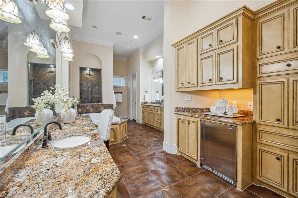 Timeless granite counters, custom cabinetry, and dual vanities create a spa-like atmosphere, complete with a beverage fridge for the ultimate indulgence.