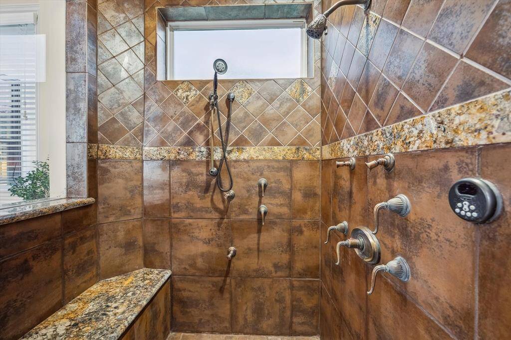 The oversized walk-in shower features rich tilework, multiple body sprays, and a built-in bench—your private wellness sanctuary.