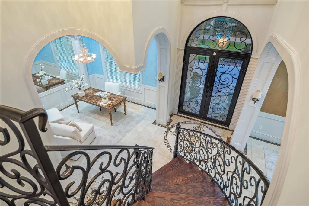 The sweeping staircase makes a grand impression with its intricate wrought iron railing, perfectly complementing the soaring ceilings and custom millwork.