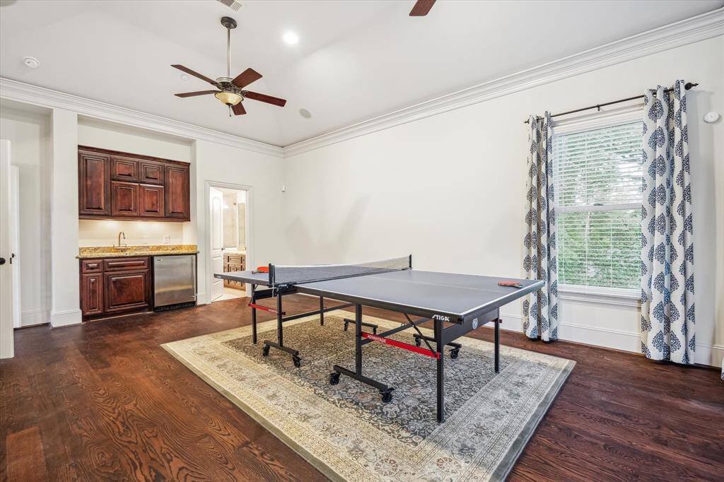 This spacious upstairs game room includes a built-in wet bar with rich cabinetry, undercounter refrigerator, and a full bath—perfect for entertaining with style and ease.