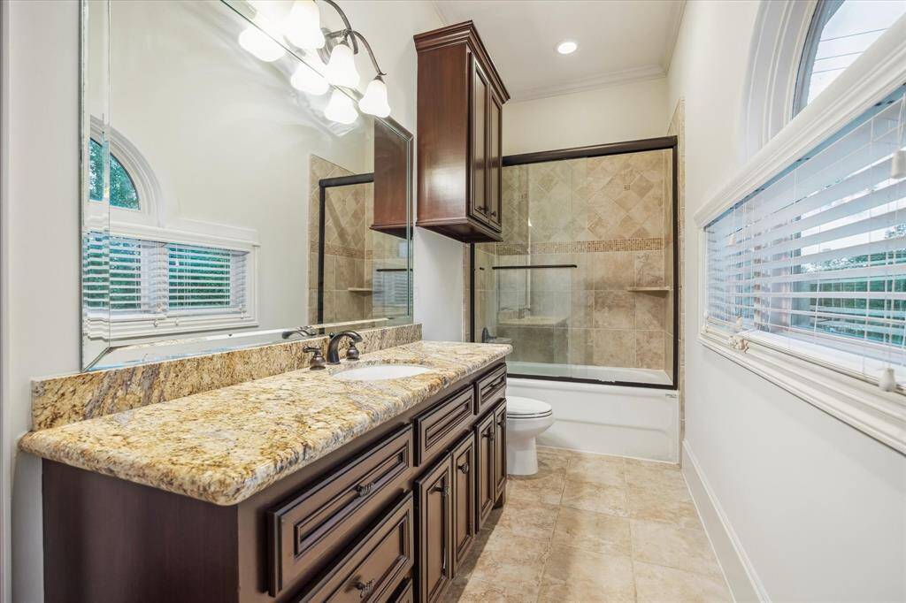 Every bedroom in this home features its own private en-suite bath, each beautifully finished with custom cabinetry, granite countertops, and designer tile surrounds like this one.