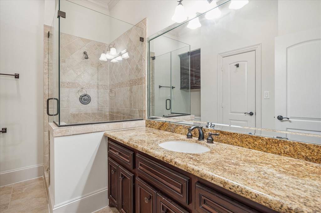 An elegant sample of the full en-suite baths found throughout—showcasing rich wood cabinetry, granite counters, and a frameless glass shower with timeless tilework.