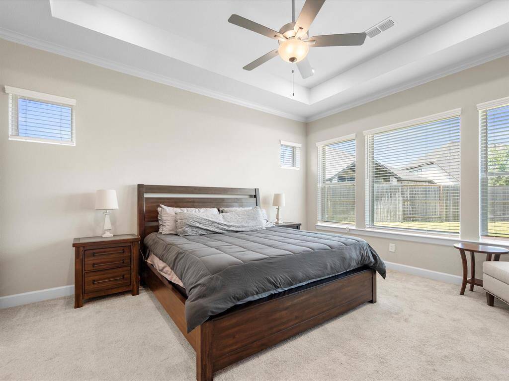 Spacious primary bedroom featuring large windows that flood the room with natural light, a tray ceiling with an elegant ceiling fan, and a cozy, inviting atmosphere. Ample space for furnishings and a comfortable sitting area.