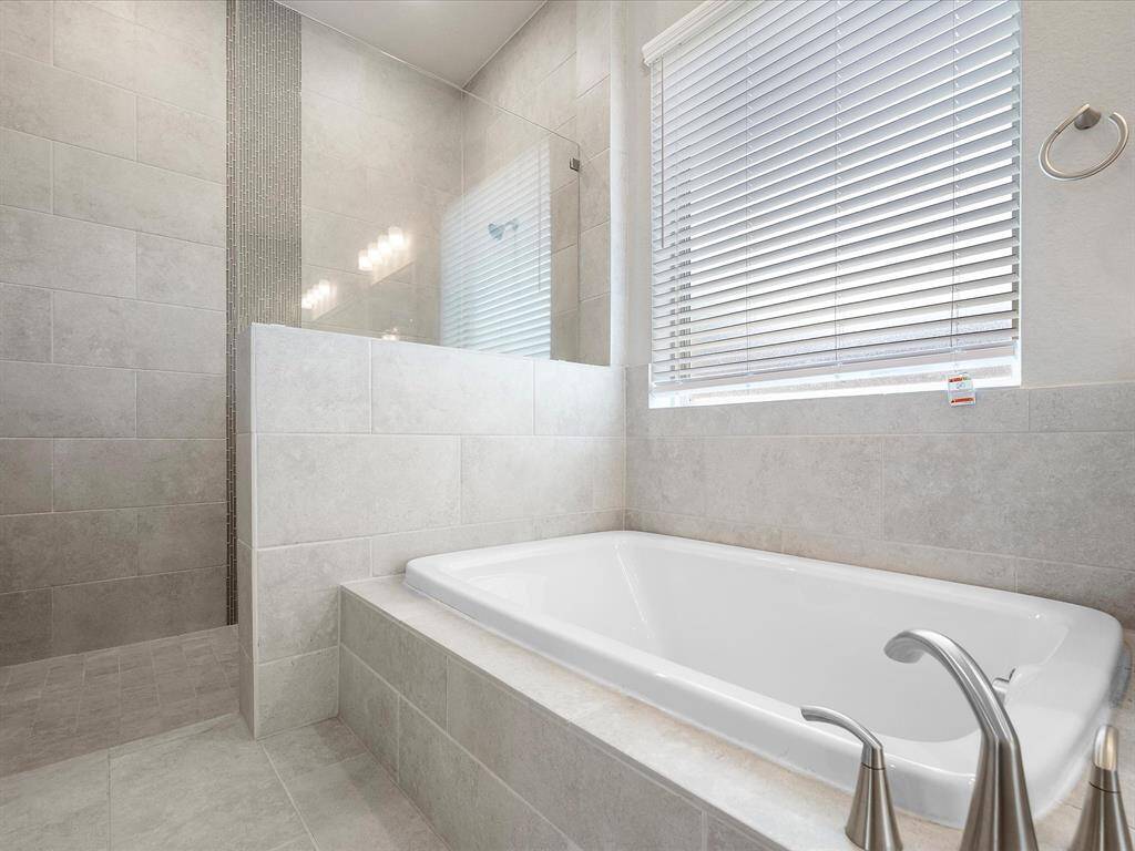 A oversized walk-in shower and separate soaking tub provide a luxurious touch, while neutral tile flooring and ample lighting create a serene, spa-like atmosphere.