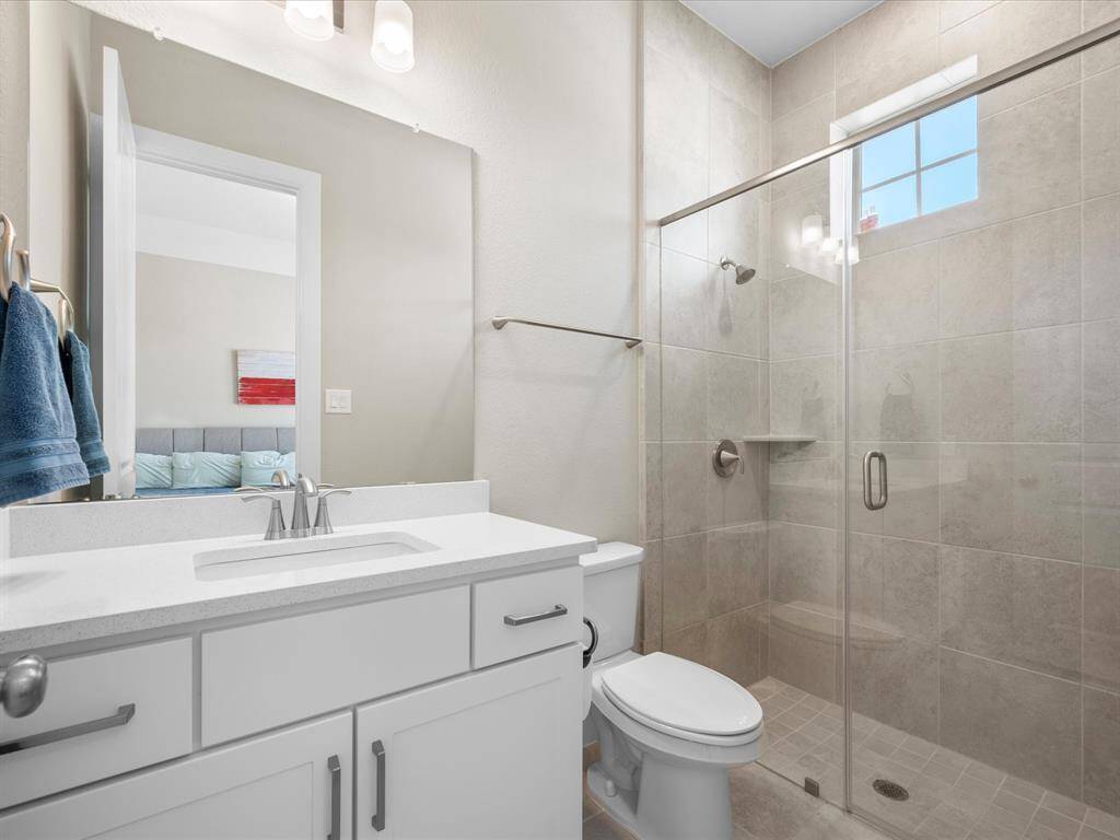 Modern en suite bathroom featuring a sleek white vanity with an under-mount sink and polished chrome fixtures. A glass-enclosed shower with light beige tile surround.