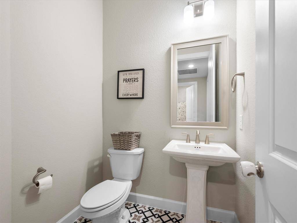 Charming half bathroom with a classic pedestal sink, sleek toilet, and eye-catching decorative tile flooring—perfectly designed for style and function in a compact space.