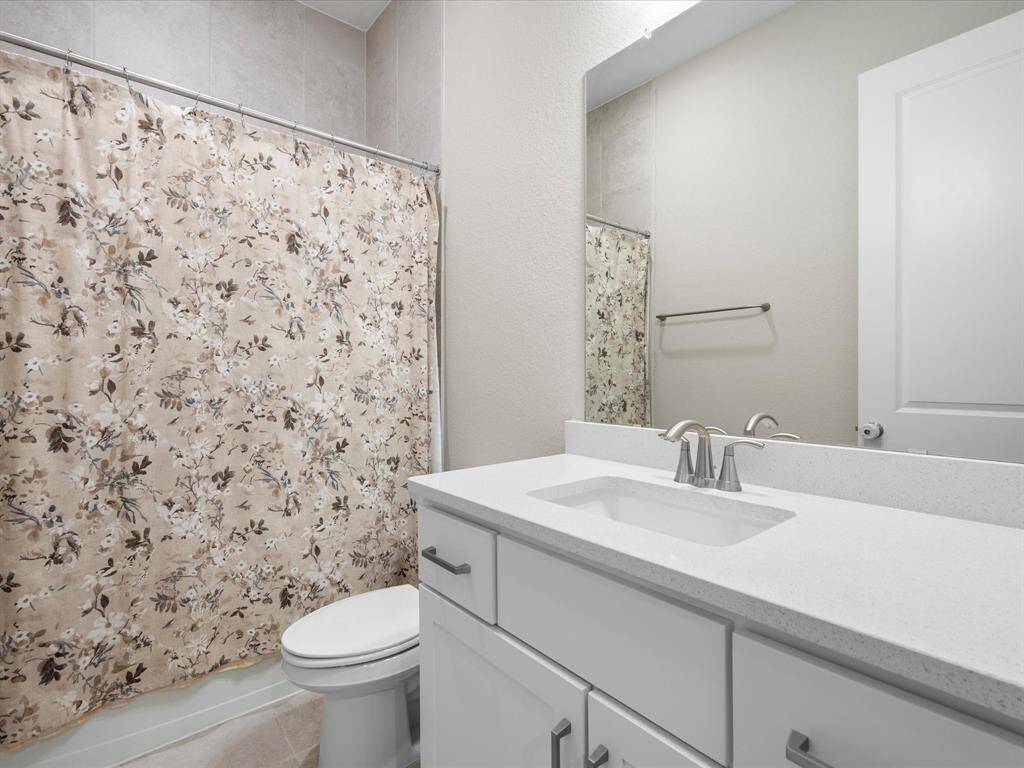 secondary bathroom with sleek quartz countertops, polished chrome fixtures and an under-mounted sink. The white cabinetry complements the modern aesthetic, while the tub/shower combo offers both style and functionality.