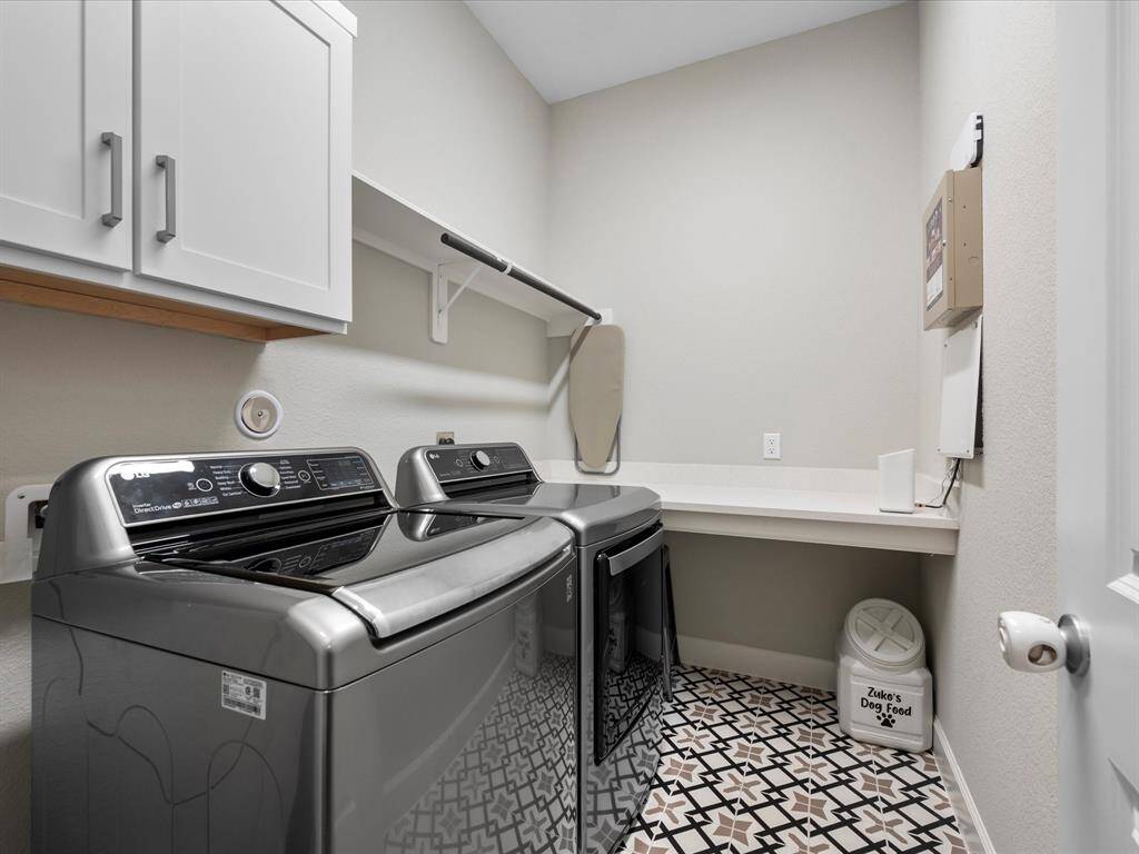 Bright and functional utility room featuring stylish decorative tile flooring. This spacious room offers plenty of overhead cabinet space for storage, a convenient folding table, and ample room for all your cleaning supplies. Additionally, a built-in rack provides a handy spot to hang clothes, making this a practical and organized space for everyday chores.