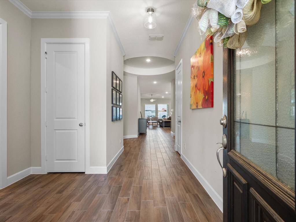 Step into an elegant entryway featuring warm wood-look tile flooring, a stunning tray ceiling with recessed lighting, and soft neutral tones that offer a welcoming and sophisticated first impression. Thoughtful architectural curves guide you into the heart of the home.