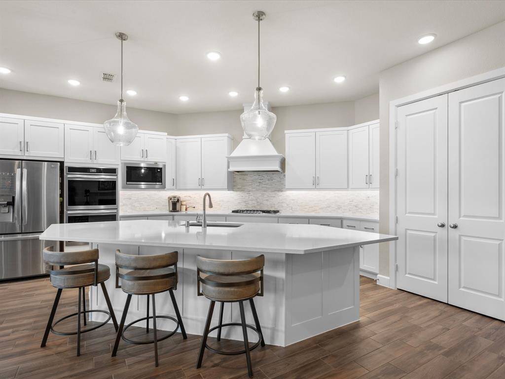 This modern kitchen showcases a spacious, thoughtfully designed layout with crisp 42'' white cabinetry, premium stainless steel appliances, and an oversized island with bar seating—perfect for casual dining or entertaining.