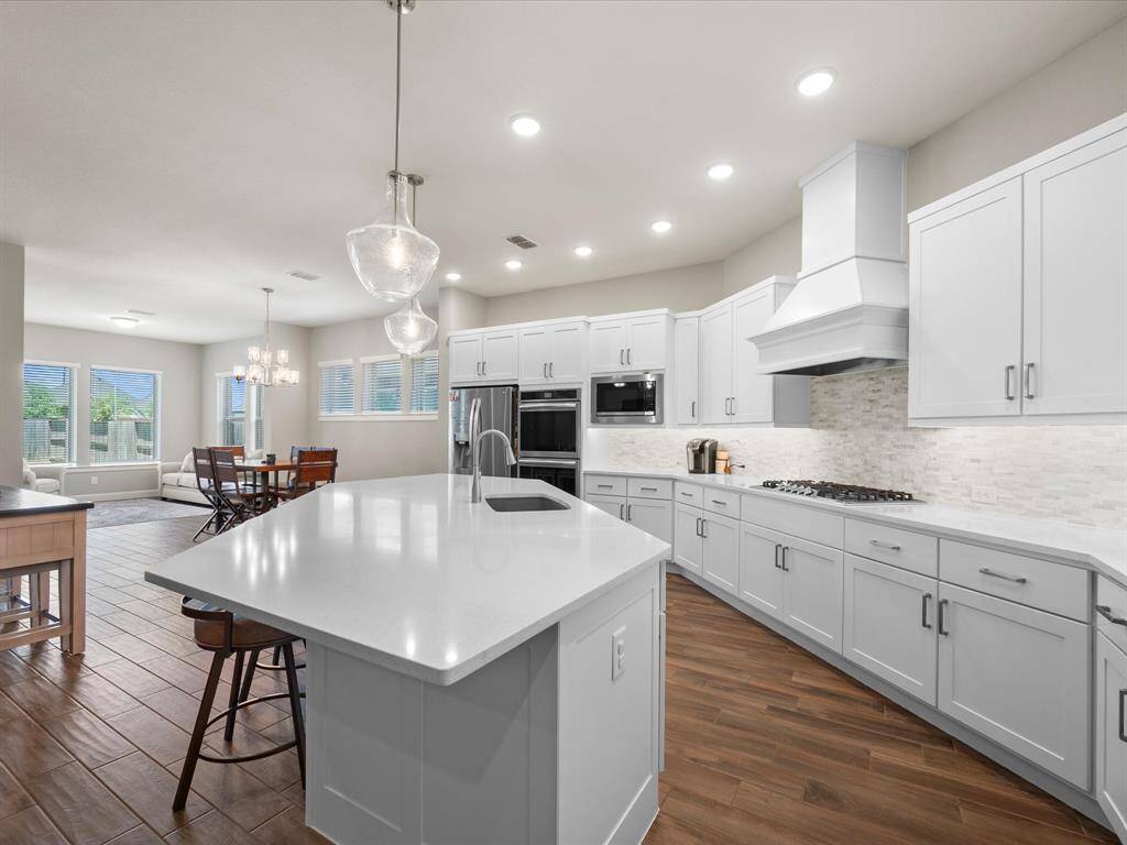 Elegant pendant lighting adds a touch of sophistication, while the wood-look tile flooring brings warmth and contrast to the bright, open space.