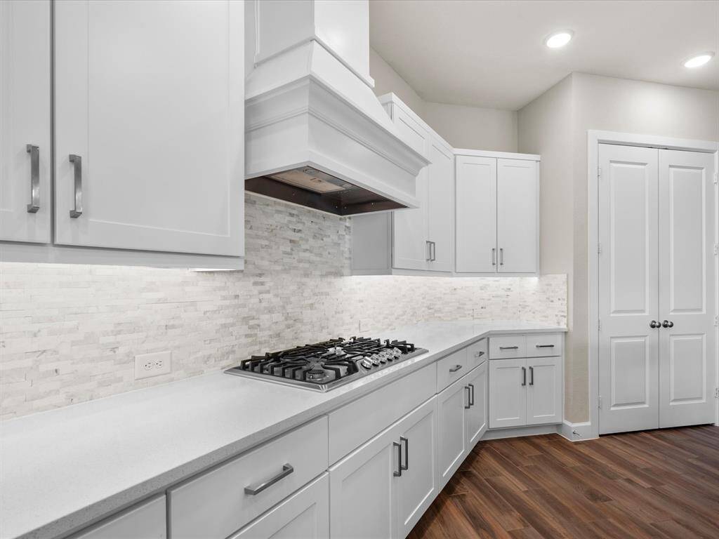 This kitchen offers a sleek gas cooktop, and a designer tile backsplash that adds texture and style. Expansive countertops provide ample prep space, while rich wood flooring lends warmth and character—an ideal blend of function and sophistication for the modern home.